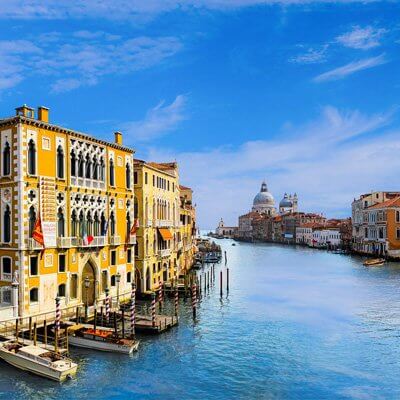 Der Canal Grande (Venedig) fließt durch die mitte des Bildes. Links sind gelbe Gebäude am Wasser. In der Ferne kann eine art Ratshaus gesehn werden.